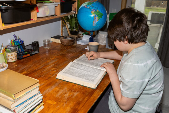 A schoolboy reading a book at a wooden table