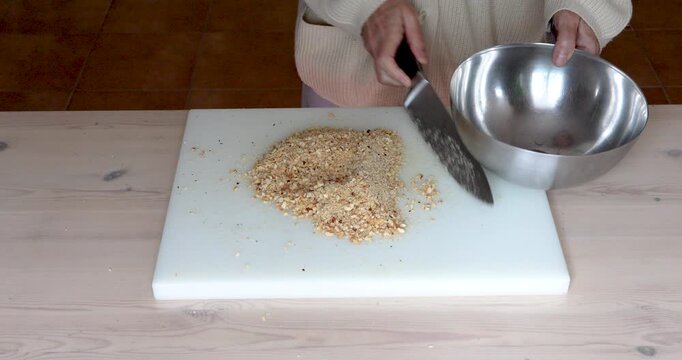Female hands transferring finely chopped roasted hazelnuts into steel bowl while preparing traditional homemade cookies.
