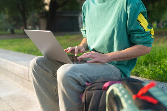Gen z guy sits with laptop in green park in Italy while travelin