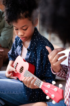 Girl learns ukulele with help from mother.