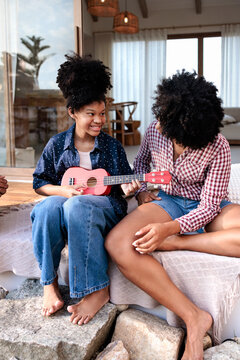 Mother and daughter share ukulele music on a sunny day.
