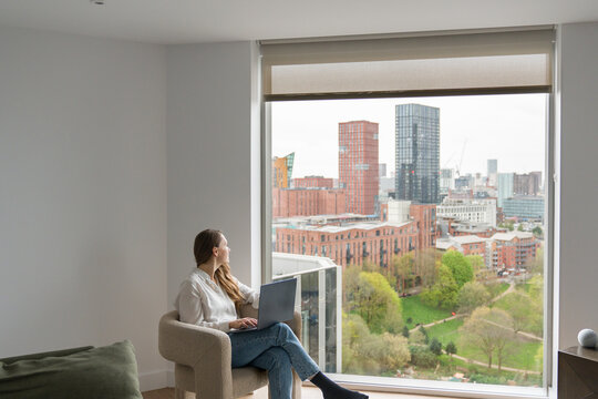 Woman With a Laptop Near a Window With City View