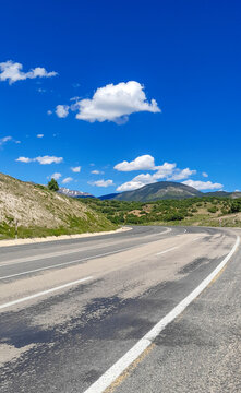 Empty asphalt road winding through mountains in Koyulhisar, Sivas, Turkey under a blue sky.