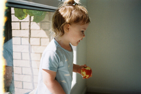 Cheeky child beside window in morning light at home with an apple