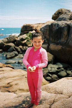 Young Girl in Pink Stinger Suit Standing Among Coastal Rocks in Bowen
