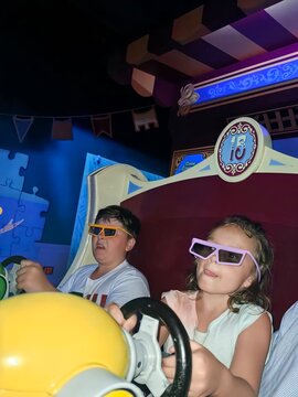 Kids in 3D glasses drive mock cars at vibrant amusement ride

