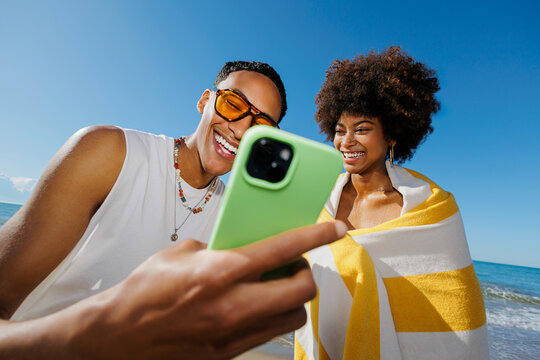 Happy friends sharing phone screen at beach vacation