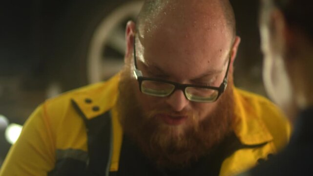 Caucasian male mechanic with glasses and a beard works alongside a female technician, reviewing a digital tablet and giving a thumbs-up. This high-energy commercial imagery represents gender diversity