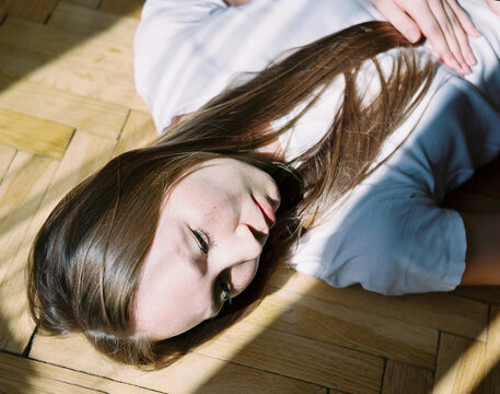 Young Woman Lying on Parquet Floor with Sunlight Streaming Across Her 