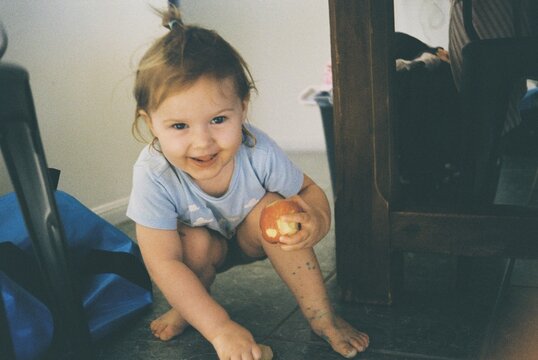 Young child hiding beneath table at home with an apple