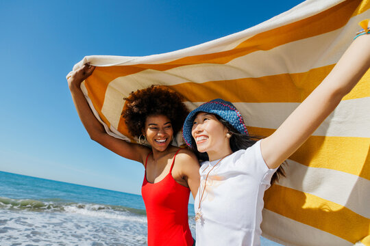 Happy friends enjoying summer day at beach holding towel