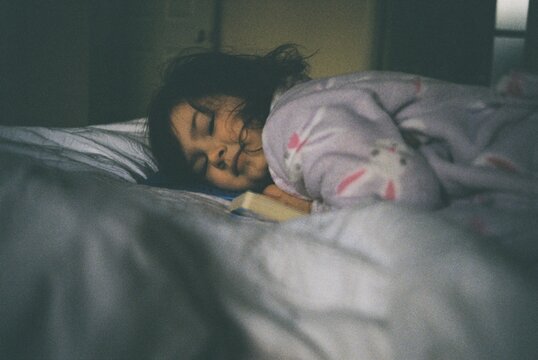 Young girl laying on her book looking towards window light.