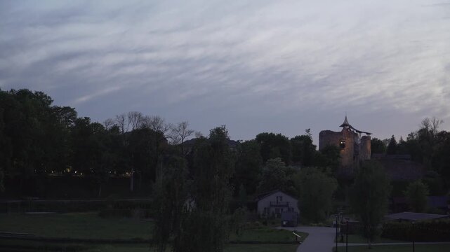 The illuminated tower of Dobele Castle stands above dark tree silhouettes under a soft twilight sky. Ideal for heritage documentaries, travel promotions, or calm cinematic transitions. 