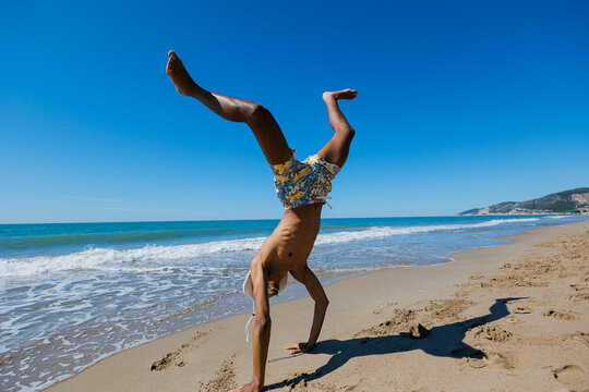 Man performing handstand on sand beach by blue sea