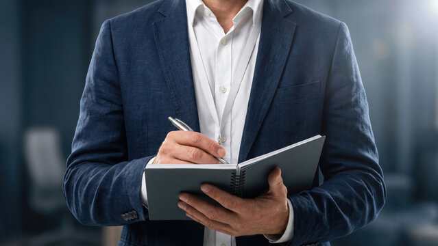 Professional businessman taking notes in a dark blue blazer with a pen and notebook.
