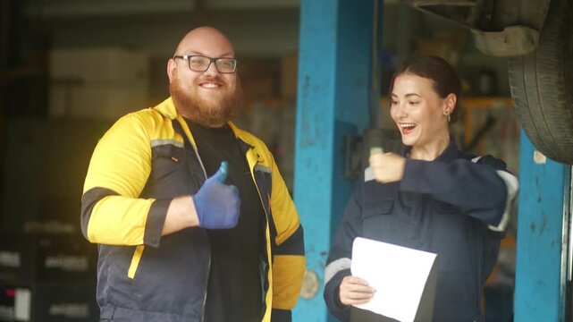 Caucasian male mechanic with glasses and a beard works alongside a female technician, reviewing a digital tablet and giving a thumbs-up. This high-energy commercial imagery represents gender diversity