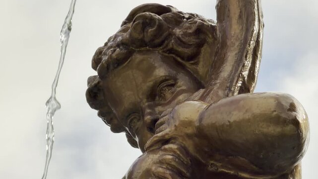A golden cherub statue spouts a clear stream of water against the bright sky. The close-up view evokes a whimsical and nostalgic feeling. This charming scene brings joy.
