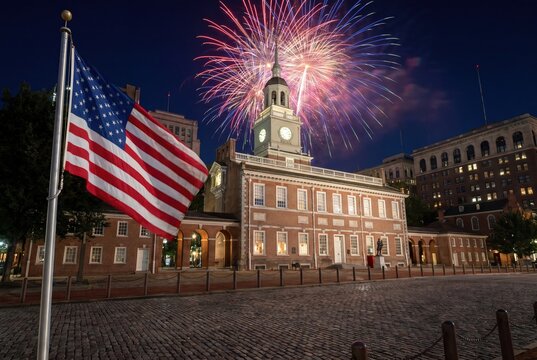 Iconic Independence Hall in Philadelphia illuminated with fireworks and an American flag waving proudly.