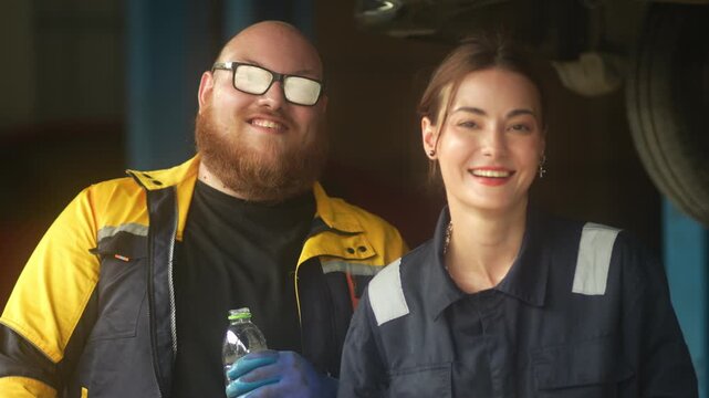 Caucasian male mechanic with glasses and a beard works alongside a female technician, reviewing a digital tablet and giving a thumbs-up. This high-energy commercial imagery represents gender diversity