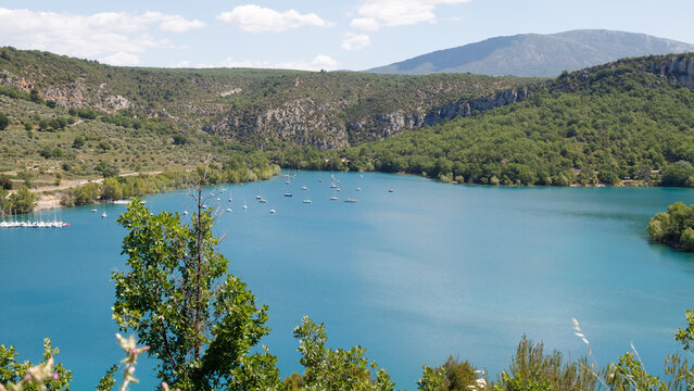Idyllischer Bergsee mit t&uuml;rkisblauem Wasser und Segelbooten inmitten gr&uuml;ner H&uuml;gel an einem Sommertag