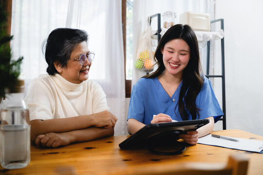 Smiling asian nurse showing digital tablet senior woman, explaining medical data older patient, consulting elderly lady digital tablet, discussing healthcare app senior patient home