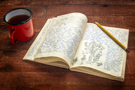 Vintage expedition journal with a metal cup of hot tea on a rustic wood table  - handwriting and drawing in pencil.from a kayak trip in Poland in summer of 1970.