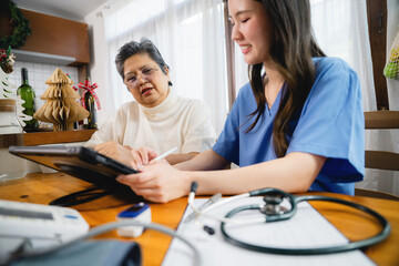 Obraz premium Serious senior asian woman talking nurse consultation at cozy home, Professional caregiver listening focused mature lady and record on tablet with medical devices foreground