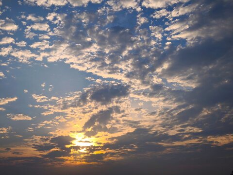 Dramatic blue sky filled with scattered altocumulus clouds illuminated by soft golden sunset light.