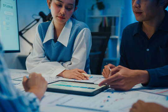 Close up asia businesspeople meeting plan analysis statistics brainstorm and tablet point graph chart employee take note in office conference room at night. Business finance partners strategy success.