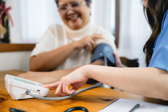 Close-up of nurse pointing at blood pressure monitor display. Calm hands hold patient's arm with cuff. Patient smiles showing trust in care. Clinical setting emphasizes professional medical check
