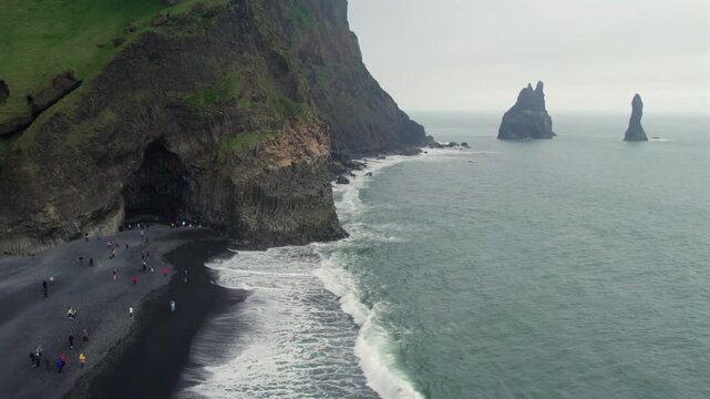 Amazing aerial view of tourists on the famous volcanic Reynisfjara black sand beach. The Reynisdrangar rock formations are visible in the ocean
