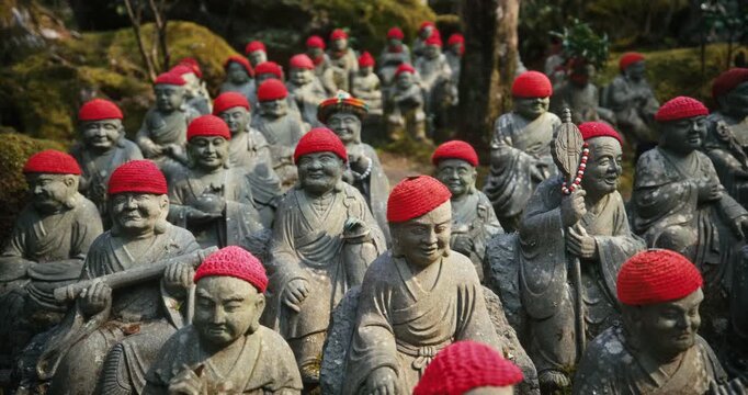 Ancient Stone Rakan Statues with Red Knit Caps at Japanese Temple - Slow Steady Cam Shot