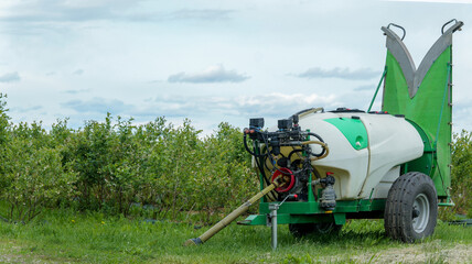 Agricultural sprayer machine in a field of blueberry bushes under a cloudy sky © shine.graphics