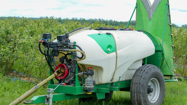 Agricultural sprayer with large tank and boom in a field of green bushes