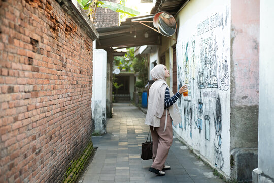 Full Length of Asian Muslim Woman Admiring Graffiti Mural Art on Wall in a Village Alleyway