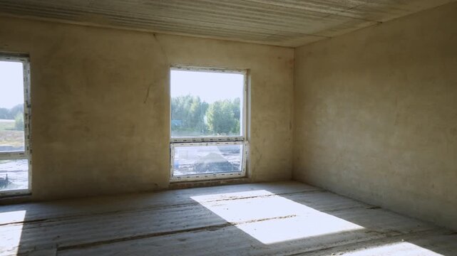 Empty concrete room under construction with sunlight moving across the floor revealing new windows and a staircase, showing progress in a new residential building