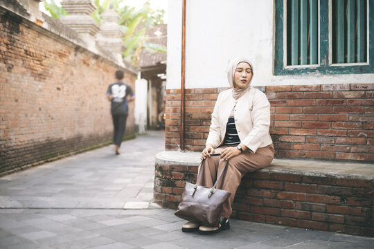 Serene Asian Muslim Woman Sitting Peacefully on Brick Ledge in a Quiet Historic Village Alley