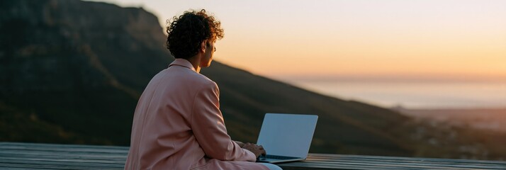 Obraz premium Young man on laptop at golden hour with mountain vista for digital nomad background and travel workspace wallpaper