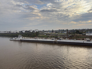 Obraz premium river tug boat with barges moored to oil terminal of port. discharging pipes connected.