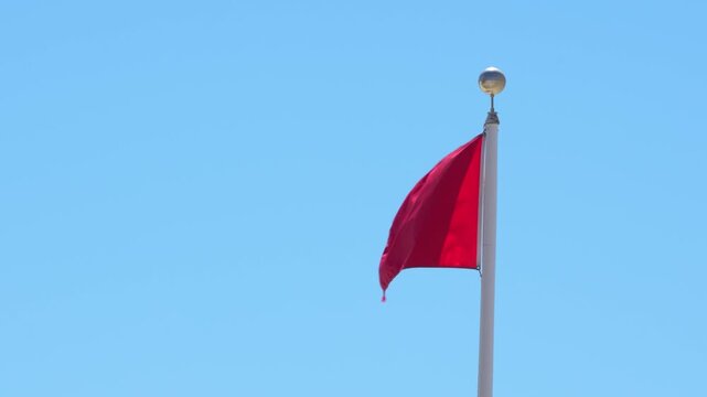 Red Flag Warning Slow Motion Waving Against Blue Sky. Signaling Hazardous Swimming Conditions. USA Panhandle of Florida. No People. Windy Closeup.