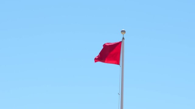 Red Flag Warning Slow Motion Waving Against Blue Sky. Signaling Hazardous Swimming Conditions. USA Panhandle of Florida. No People. Windy Wide.