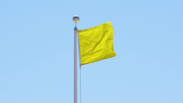 Yellow Flag Warning Waving Against Blue Sky. Signaling Hazardous Swimming Conditions. USA Panhandle of Florida. No People. White Pole Windy Closeup