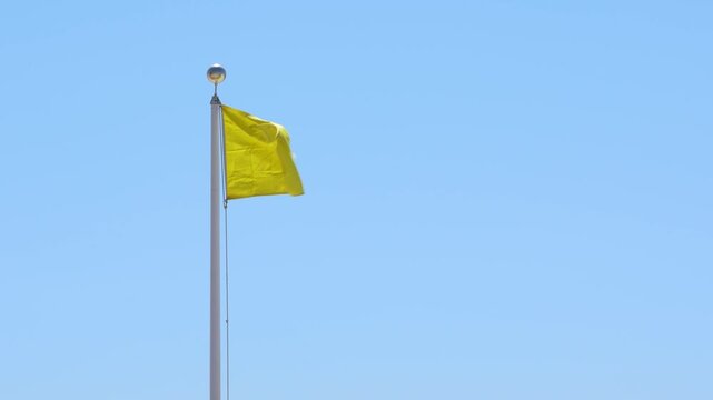 Yellow Flag Warning Slow Motion Waving Against Blue Sky. Signaling Hazardous Swimming Conditions. USA Panhandle of Florida. No People. Windy Closeup.