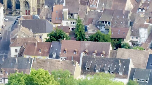 Thann, France - August 12 2025 : The Gothic Collegiale Saint-Thiebaut collegiate church with its tall openwork stone spire and glazed tile roof rising above the old town rooftops in Alsace