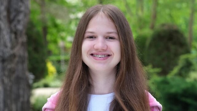 Portrait of caucasian happy teenage girl smiling showing teeth with dental braces. Positive teen outdoors looking at camera
