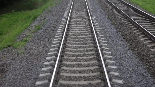 Railway tracks viewed from a moving train, showcasing the continuous progression of tracks, gravel, and surrounding greenery along the route