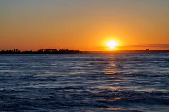 Sunset glowing on the horizon over rippling water at dusk