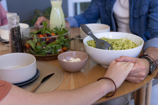 Couple clasping hands at home table with denim top, bracelet, watch, salad bowl, copy space