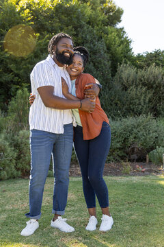 African American couple hugging on park lawn in layered shirts white sneakers bracelet lens flare