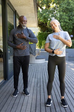 Senior couple standing on home deck placing hands on chest and abdomen, wearing watch and sneakers